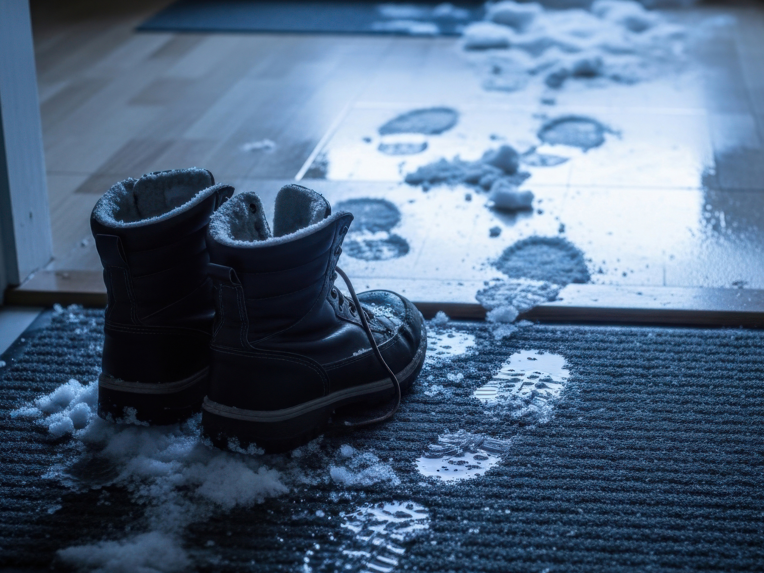 Bottes couvertes de neige qui s’apprêtent à laisser des traces dans l’entrée, idéales à déposer sur un tapis absorbant pour éviter la neige fondue au sol